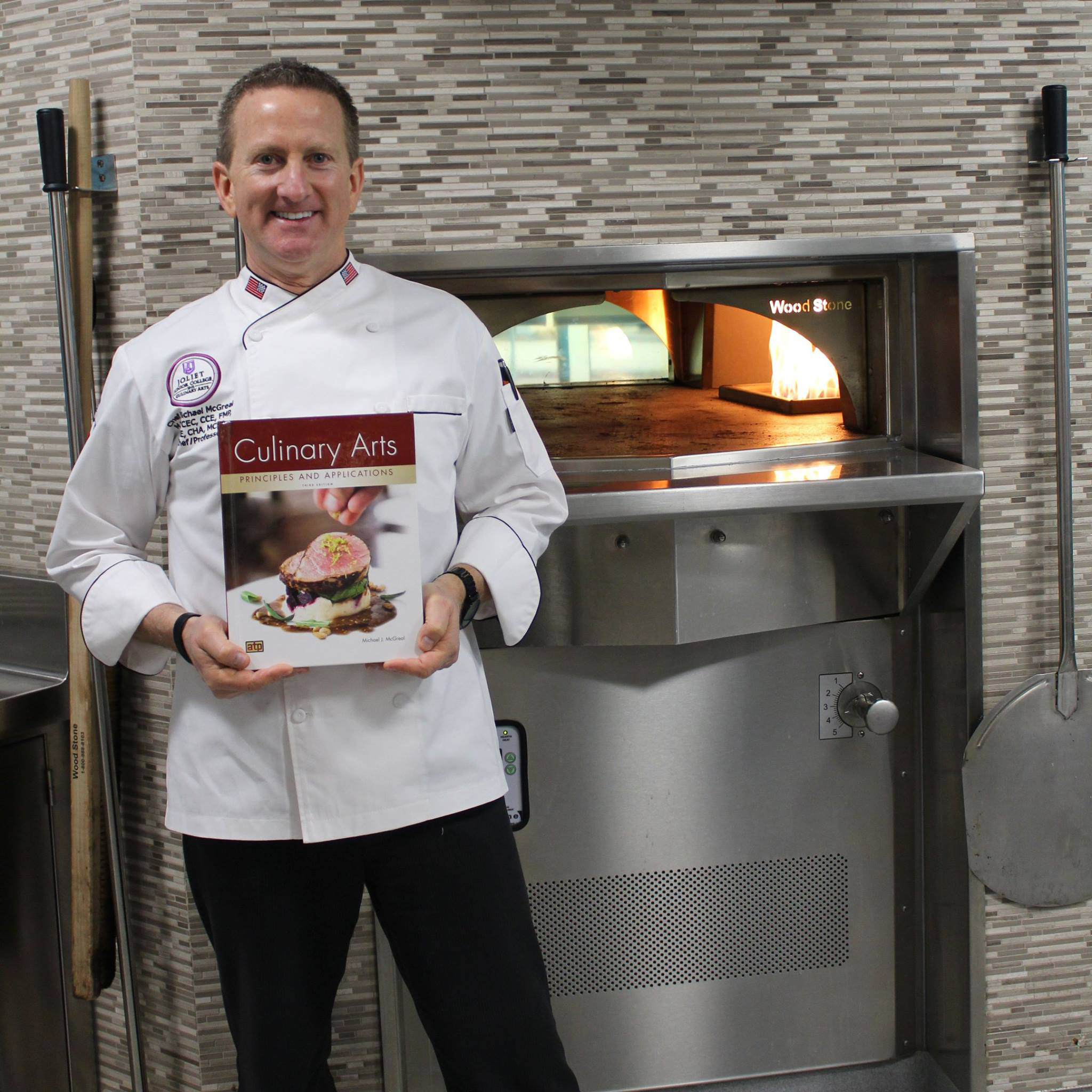 Chef Mike McGreal holding a copy of his textbook, "Culinary Arts Principles and Applications."