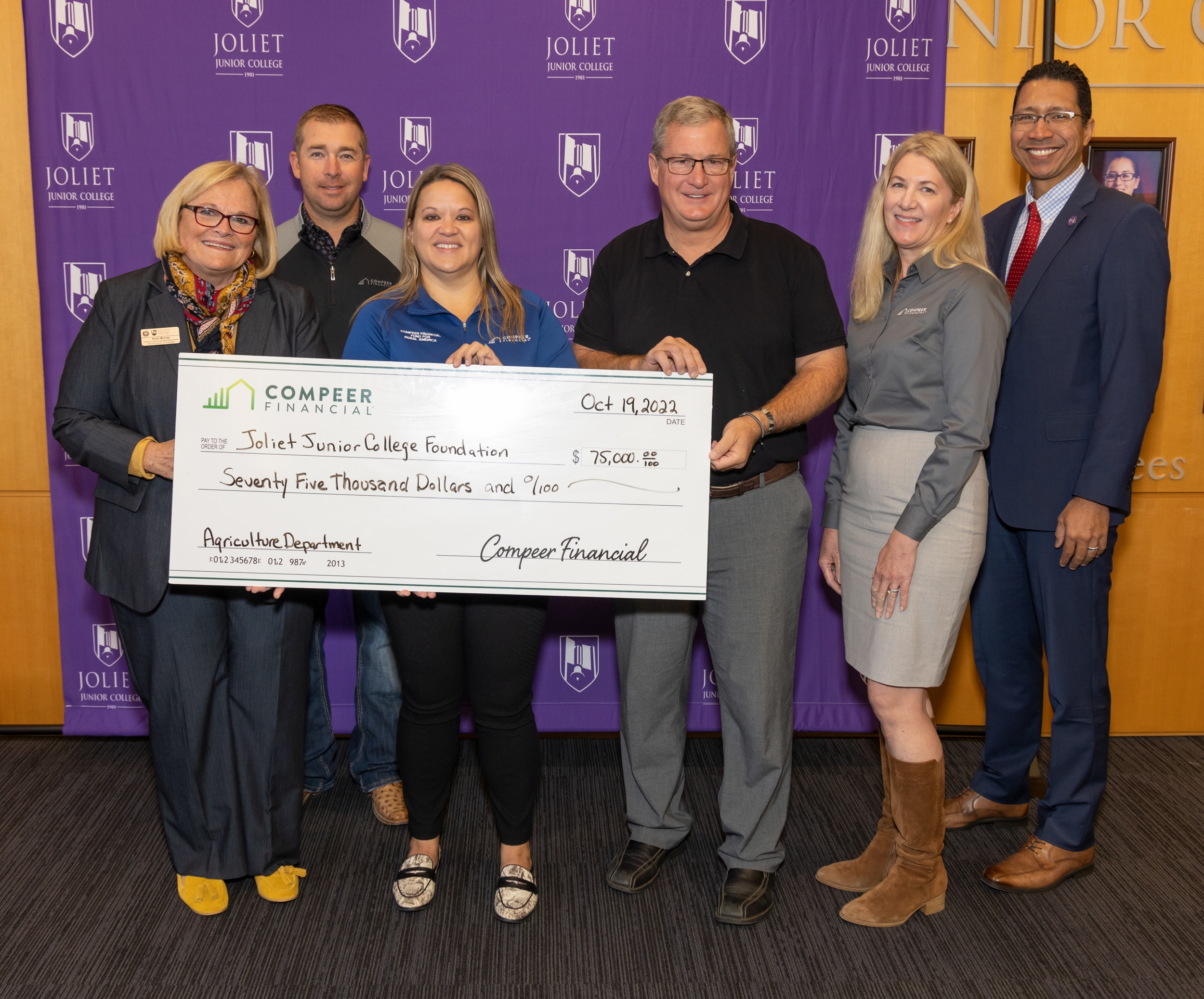 six people pose for photo with big check in front of purple JJC backdrop