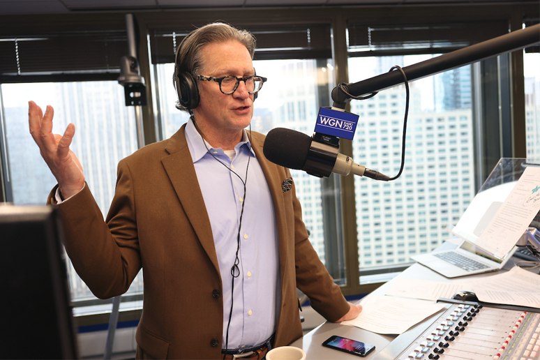 John Williams stands and talks into microphone in radio studio
