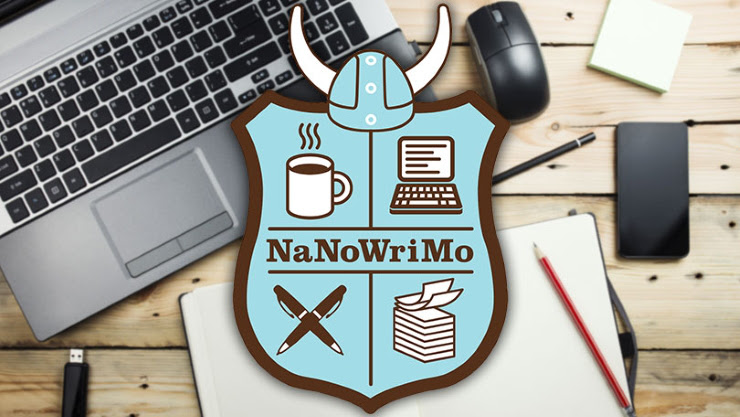 NaNoWriMo logo on top of photo of laptop, mouse, notebook and writing utensils on table