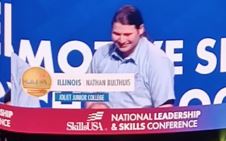 screen showing Nathan Bulthuis atop podium with name, state and school labeled (Illinoi Nathan Bulthuis Joliet Junior College) and SkillsUSA logo and National Leadership & Skills Conference at bottom