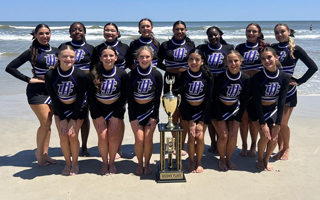 cheerleading team poses for photo on beach with trophy