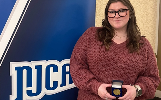 Madi Lave poses for photo in front of NJCAA banner while holding medal