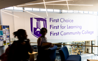 people walking in hallway with decal on wall in background that says first choice first for learning first community college