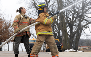 two people hold and operate fire hose