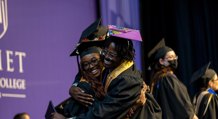 graduates embrace on stage 