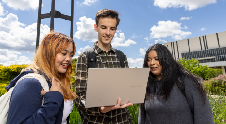 three students look at a laptop outside 