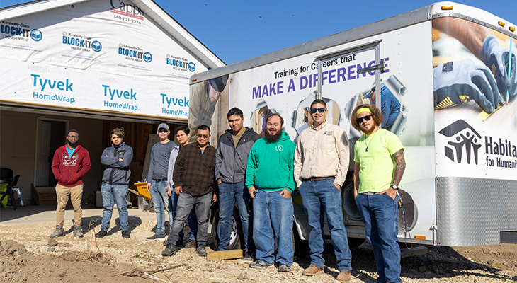 nine people at home construction site in front of HVAC trailer