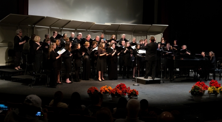 singers stand on risers while singing on stage