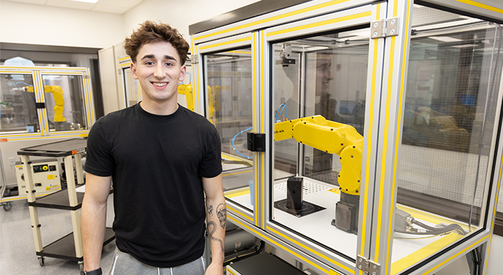Cole Gerovac poses for photo in front of robotic arm