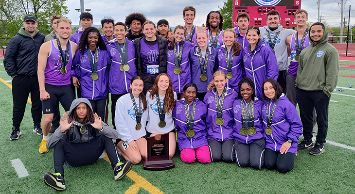 track and field athletes pose for photo outdoors with medals and trophy