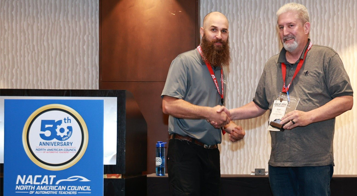 two people shake hands while posing for photo during award ceremony