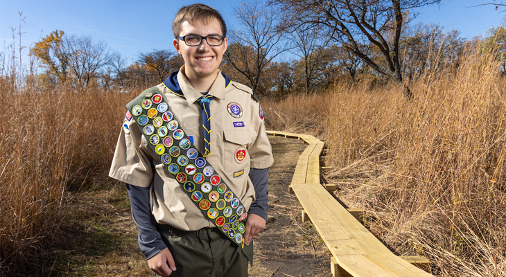 Jacob Schmidt in Eagle Scout uniform poses for photo outdoors on nature trail