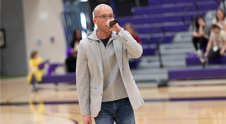 Brian Fruits-Esparza stands in gymnasium and speaks into microphone