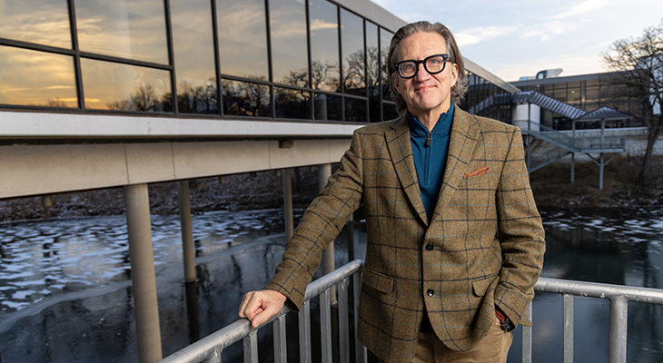 John Williams poses for photo outdoors with building, lake and sky in background