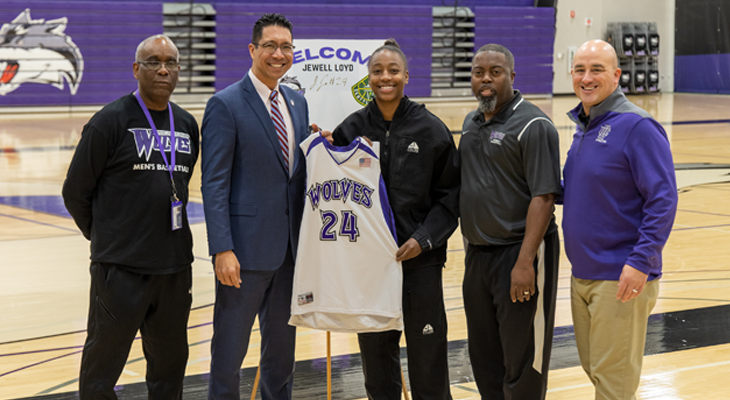 five people pose for photo with second and third holding basketball jersey